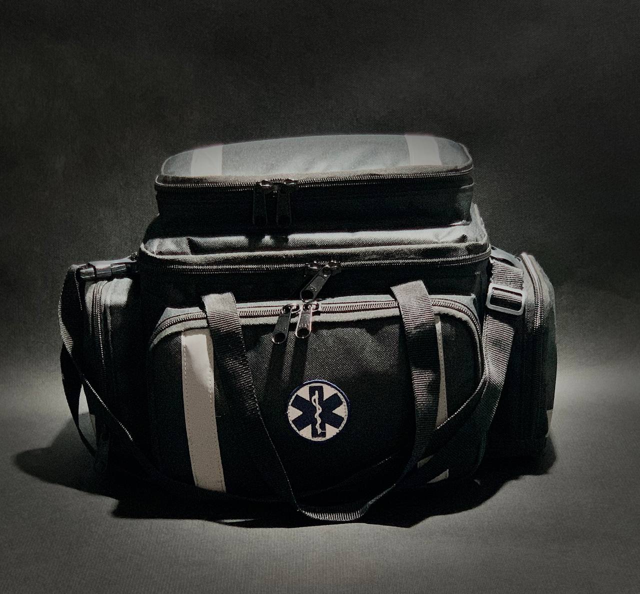 bolsa de APH. Imagem frontal, bolsa na cor preta, bordado da Cruz da Vida e faixas refletivas